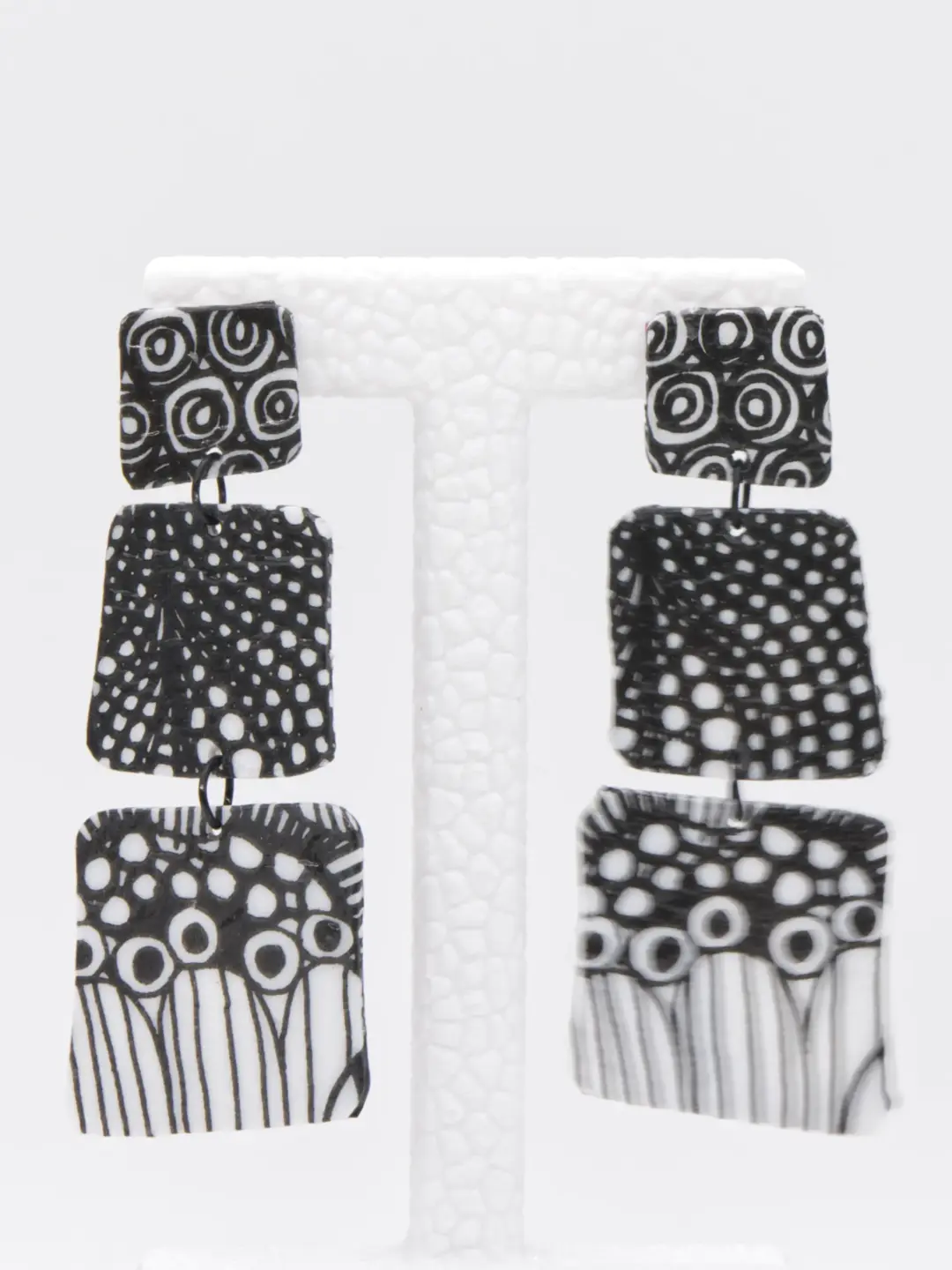 Black-and-white geometric patterned dangling earrings on display stand