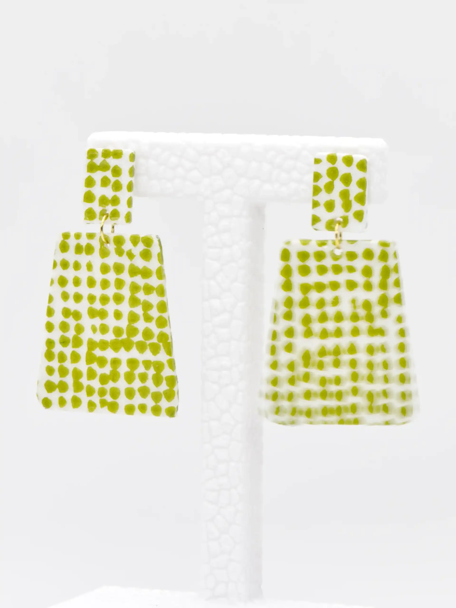 Green polka-dot rectangular drop earrings on white display