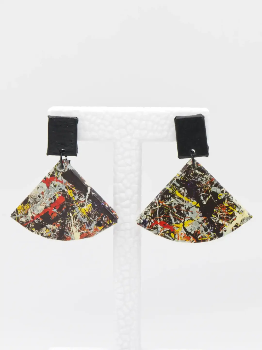 Colorful abstract fan-shaped earrings on a white display stand