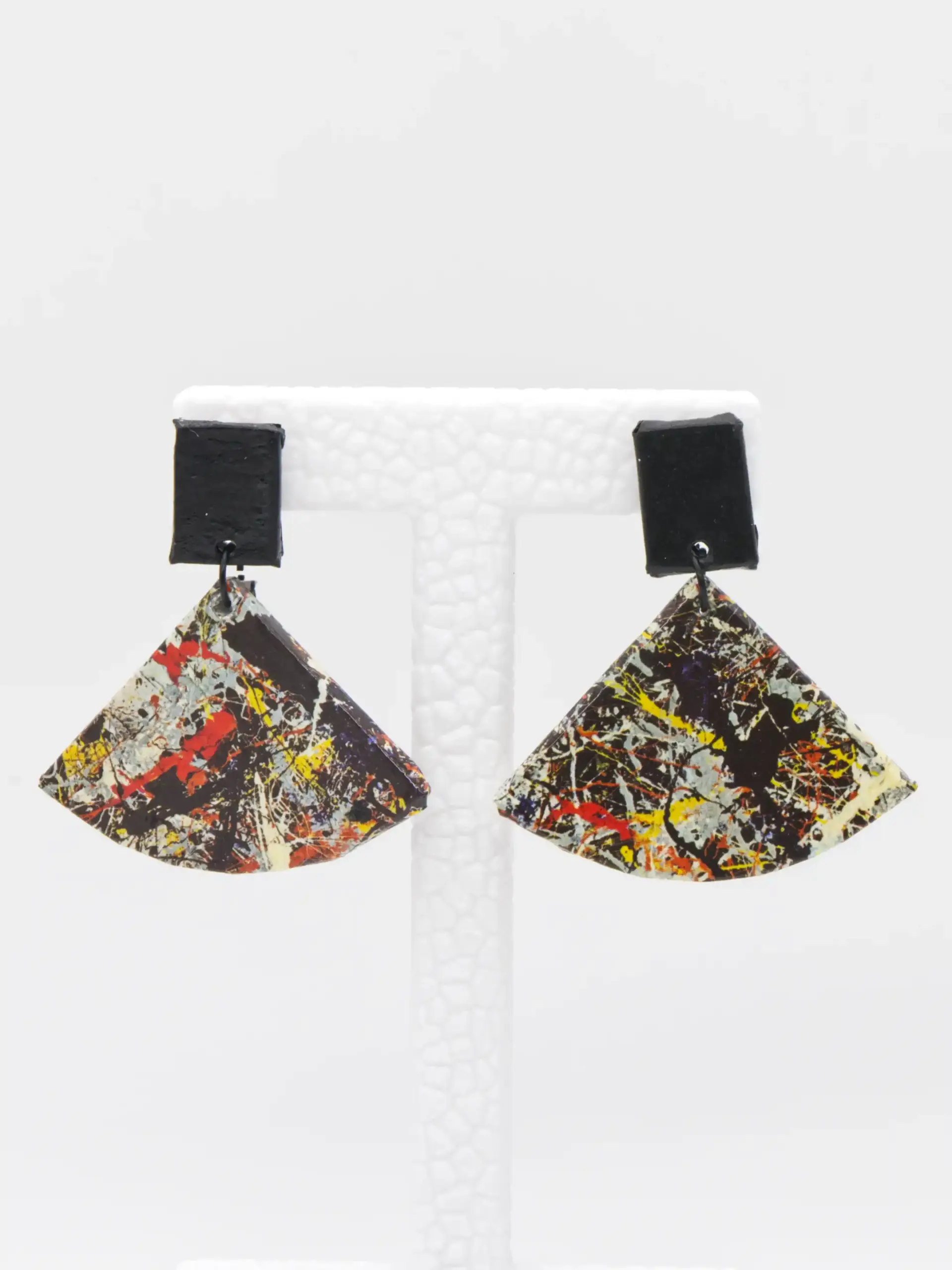 Colorful abstract fan-shaped earrings on a white display stand