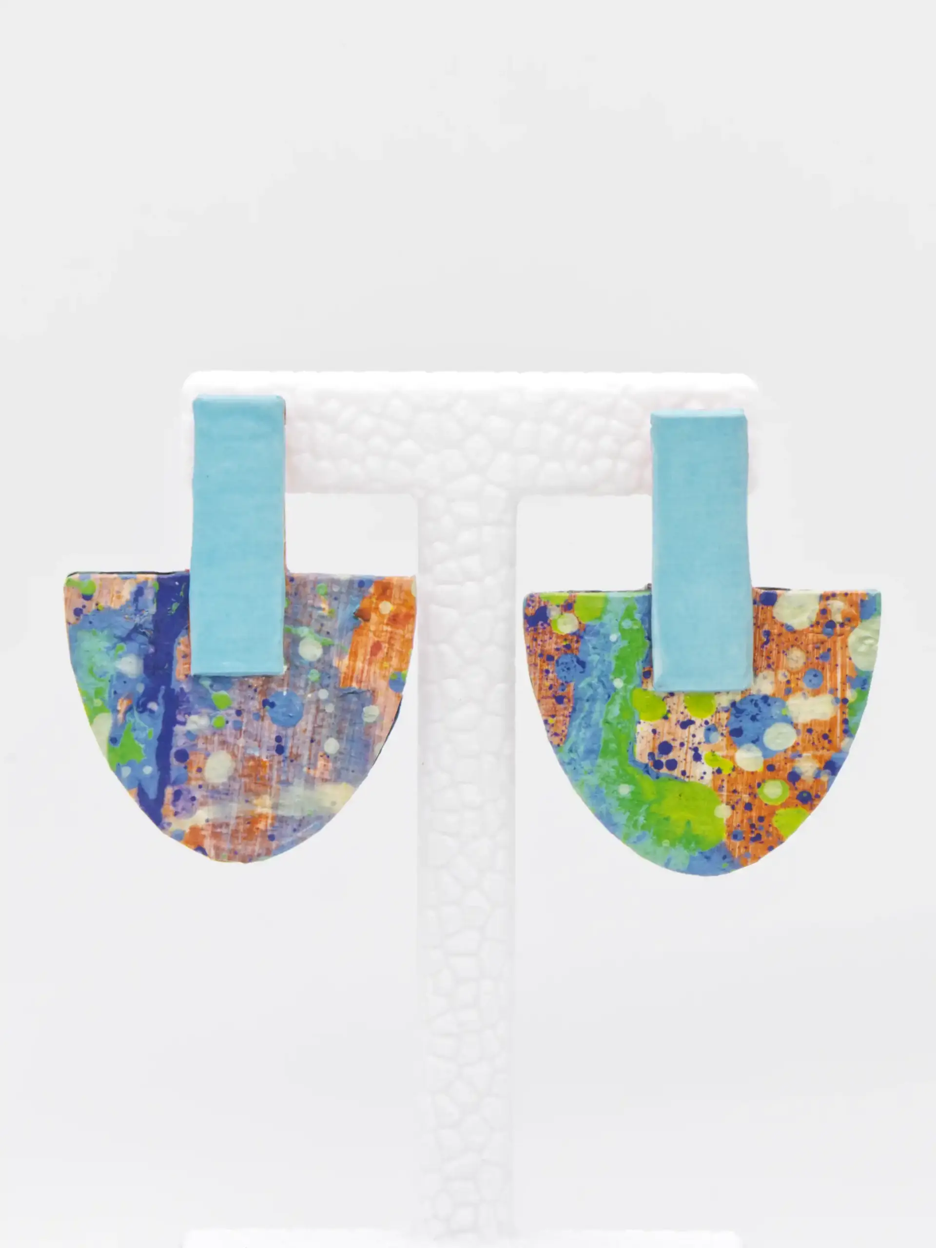Colorful abstract U-shaped earrings on a white display stand.