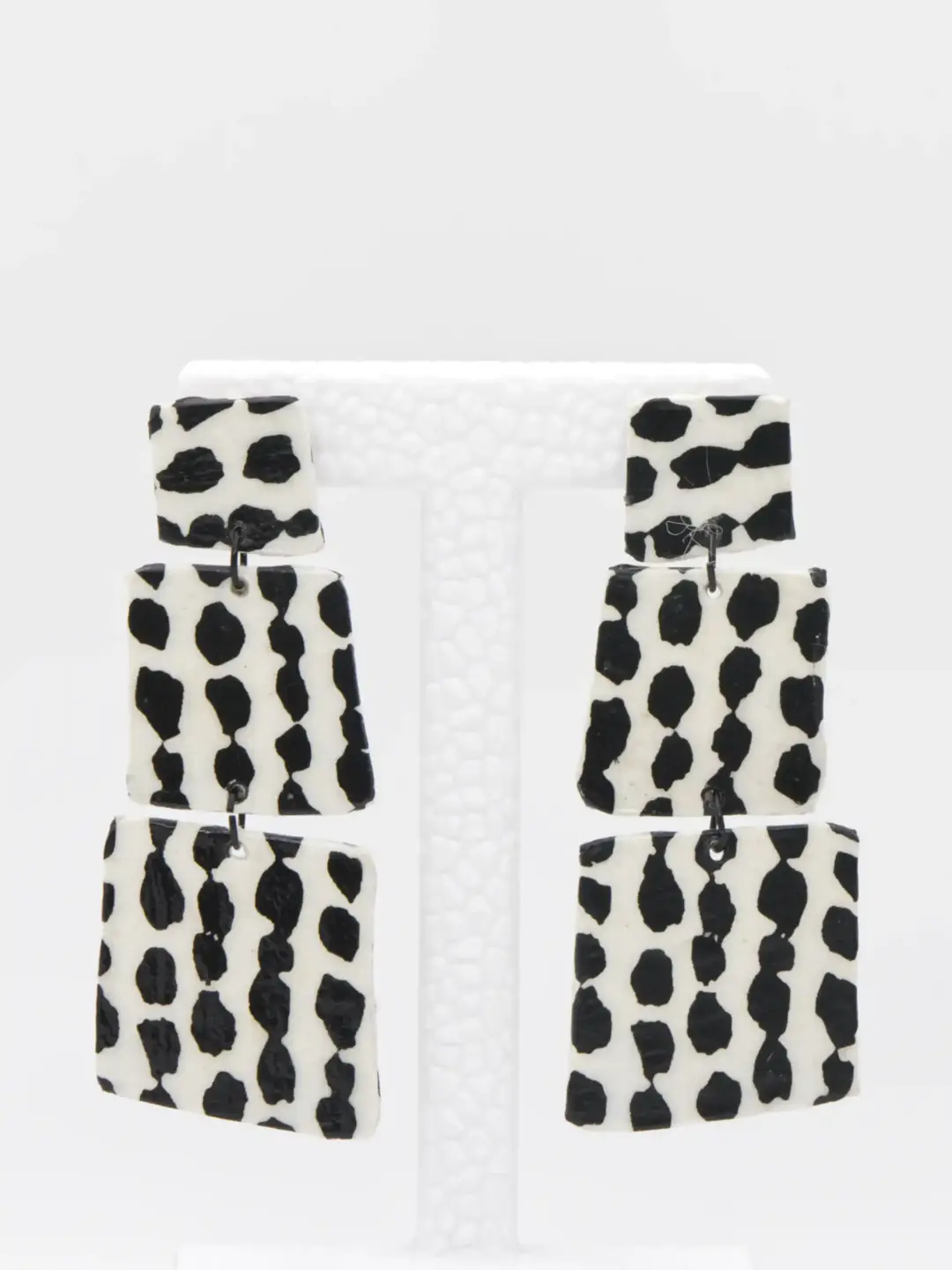 Black-and-white cow-print dangling earrings on display stand