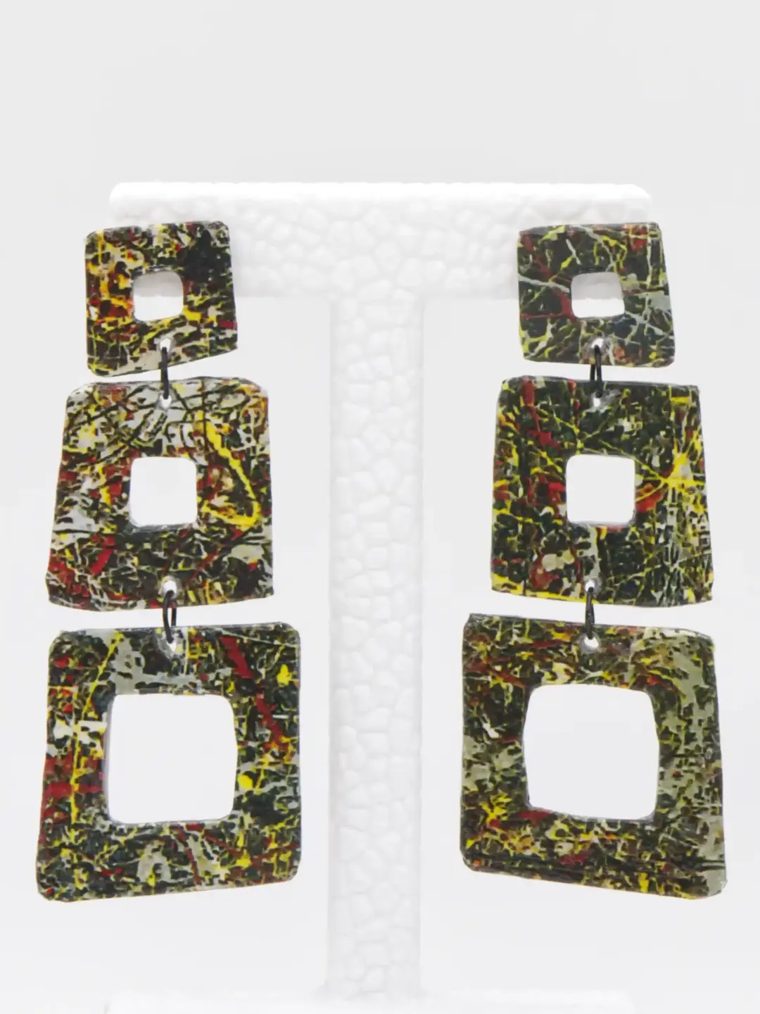 Multicolored square dangling earrings on white display stand
