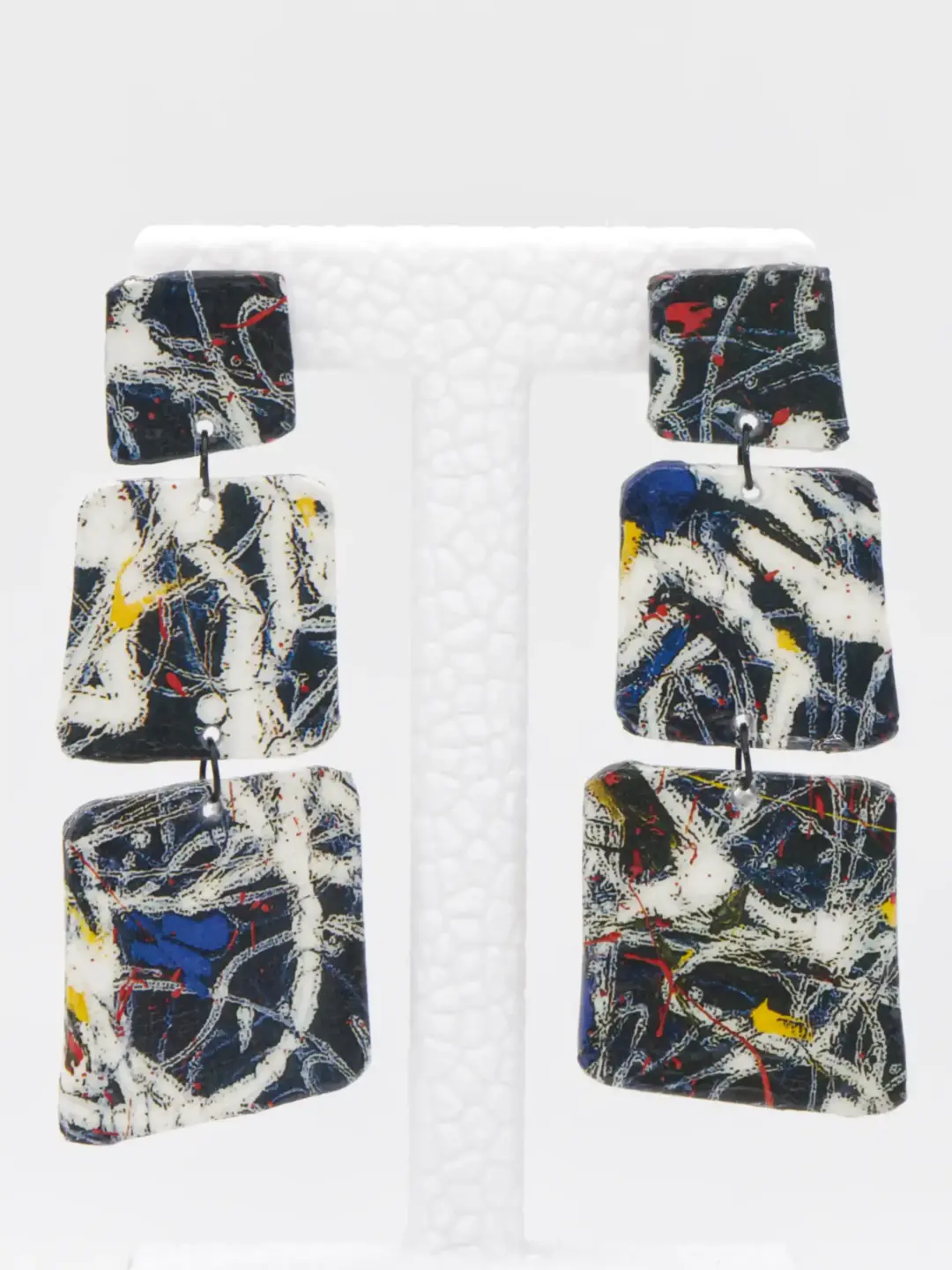 Abstract patterned geometric dangling earrings on white display stand