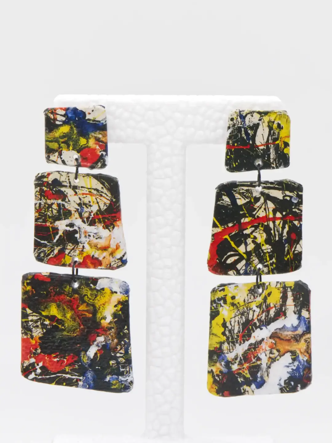Abstract paint-splatter rectangular dangle earrings on display stand